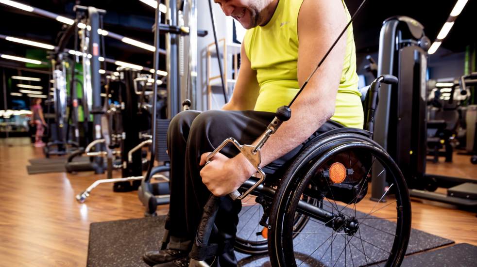 Joining a gym man in wheelchair using fitness equipment
